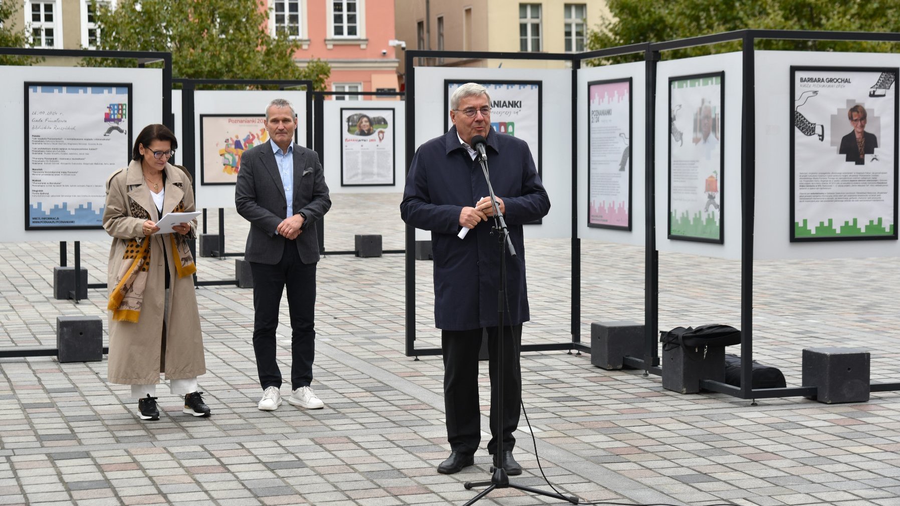 Zdjęcie przedstawiaosoby biorące udział w konferencji. Przy mikrofonie stoi przewodniczący rady miasta. Za jego plecami znajduje się wystawa.