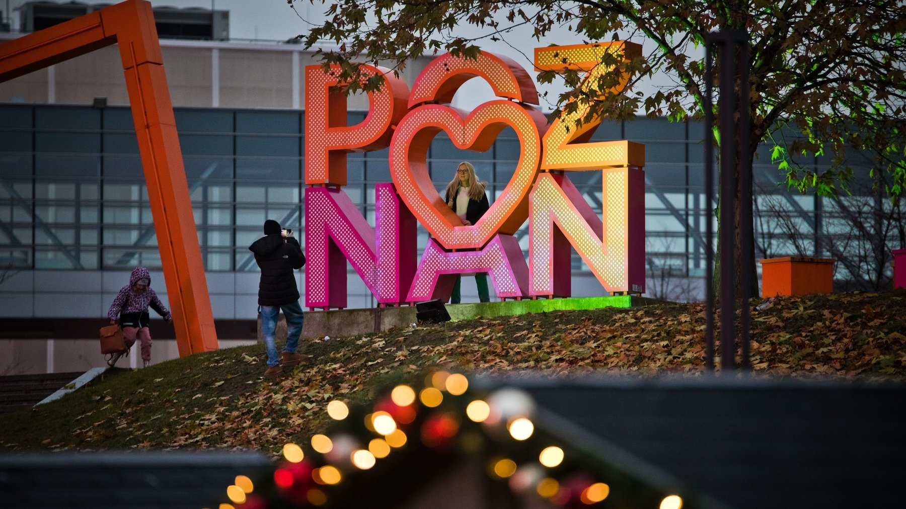 Zdjęcie przedstawia ozdobny napis Poznań i ludzi fotografujących się przy nim.