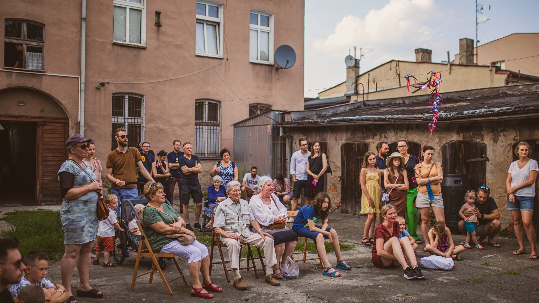 Na zdjęciu grupa ludzi na podwórku kamienicy