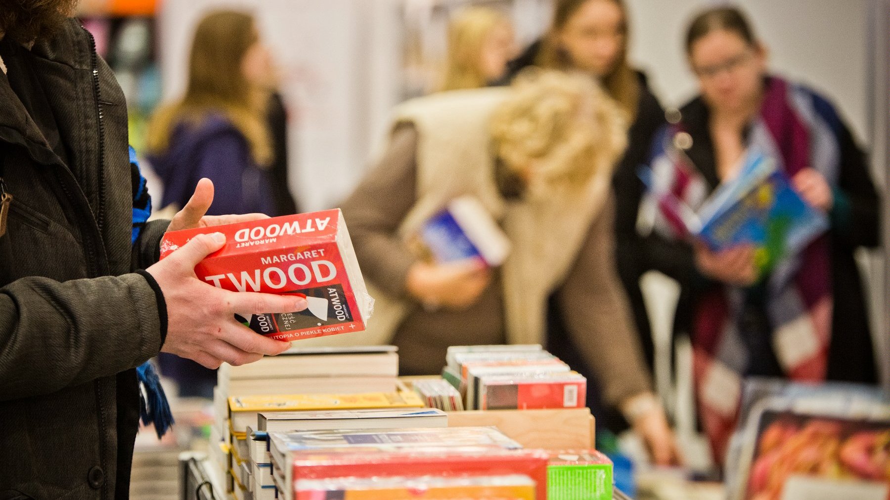 Osoba trzyma książkę Margaret Atwood. Inne Osoby i książki są rozmazane