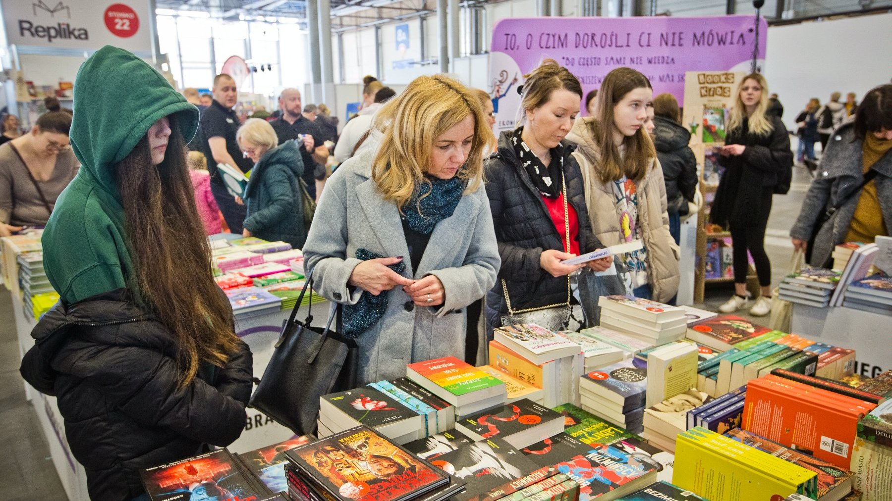 Kilka kobiet stoi przed stołem na którym położone są książki