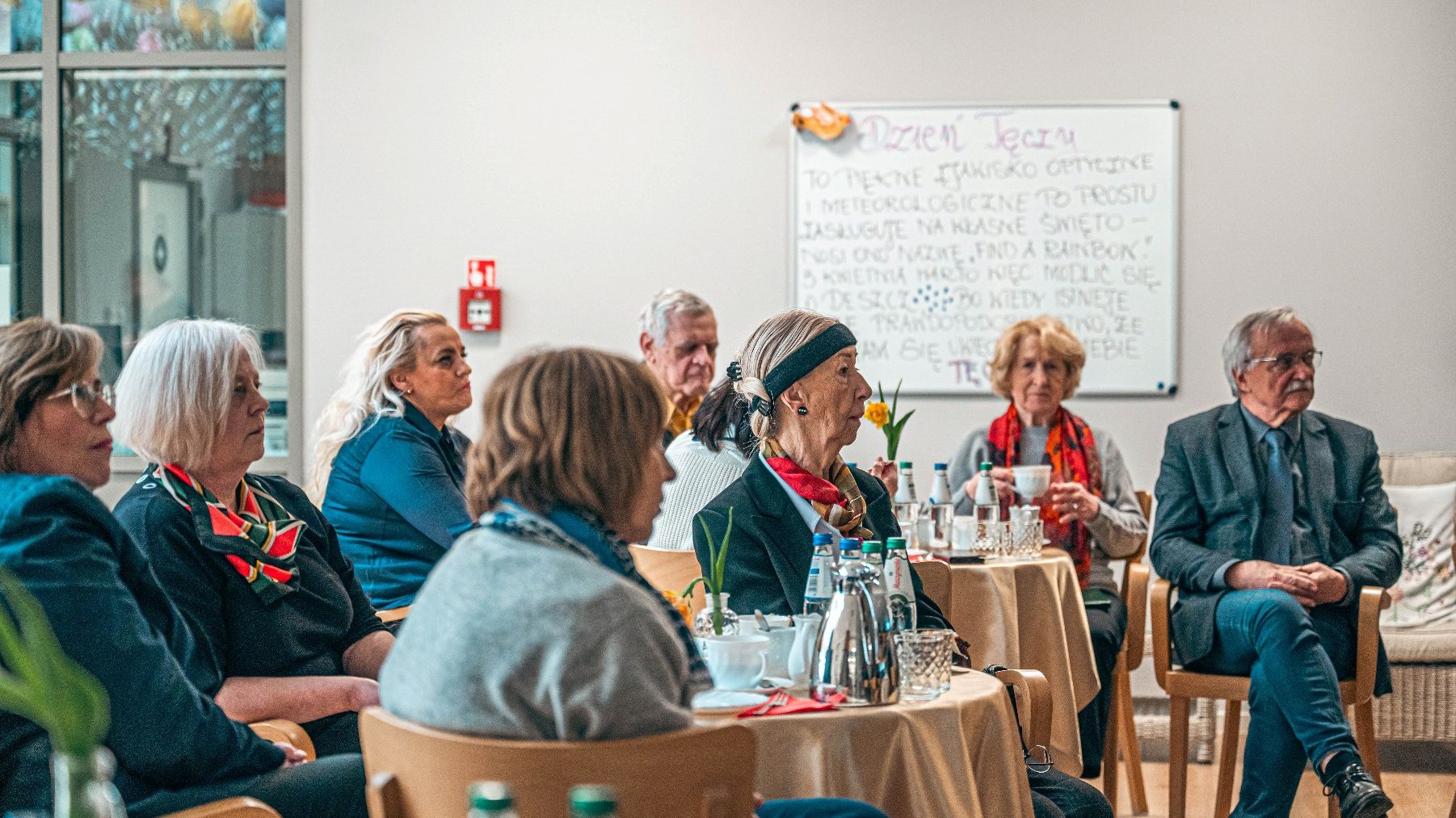 Na zdjęciu ludzie przy stolikach, słuchający prezentacji