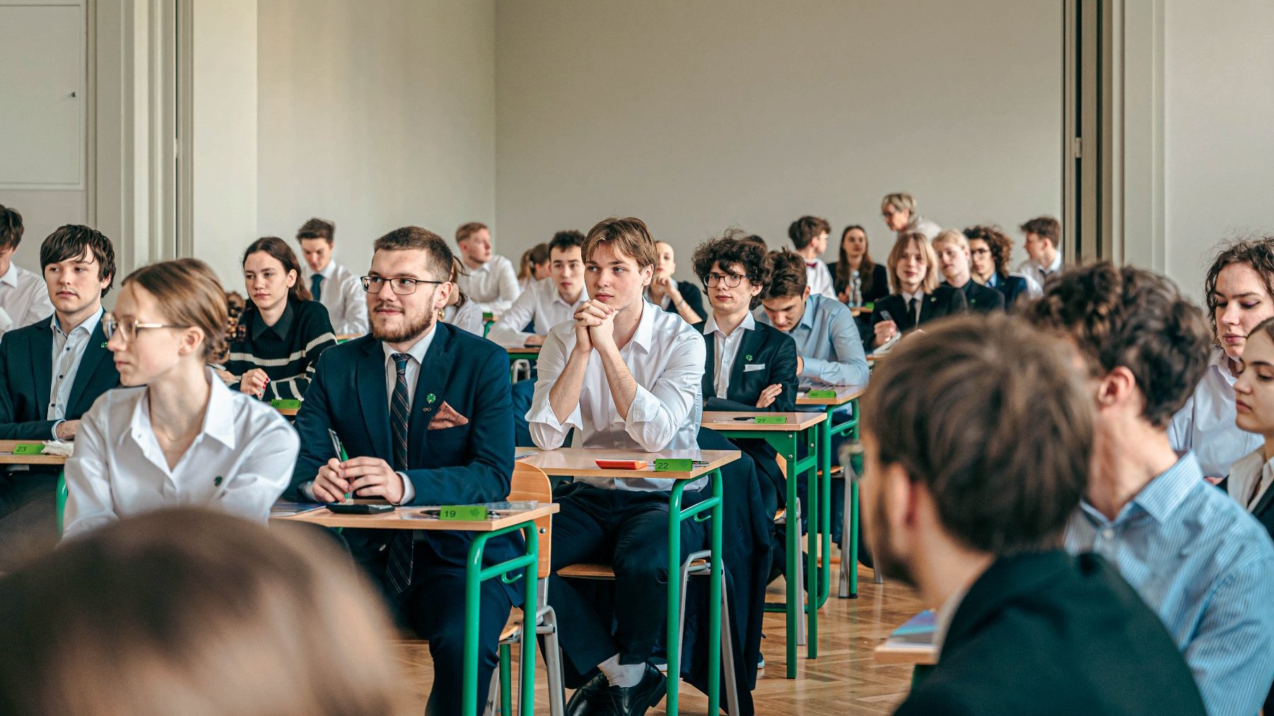 Zdjęcie przedstawia maturzystów siedzących w ławkach.