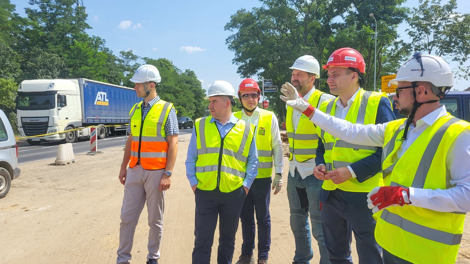 Na zdjęciu grupa osób rozmawiających ze sobą na placu budowy, mężczyzna pokazuje na coś ręką