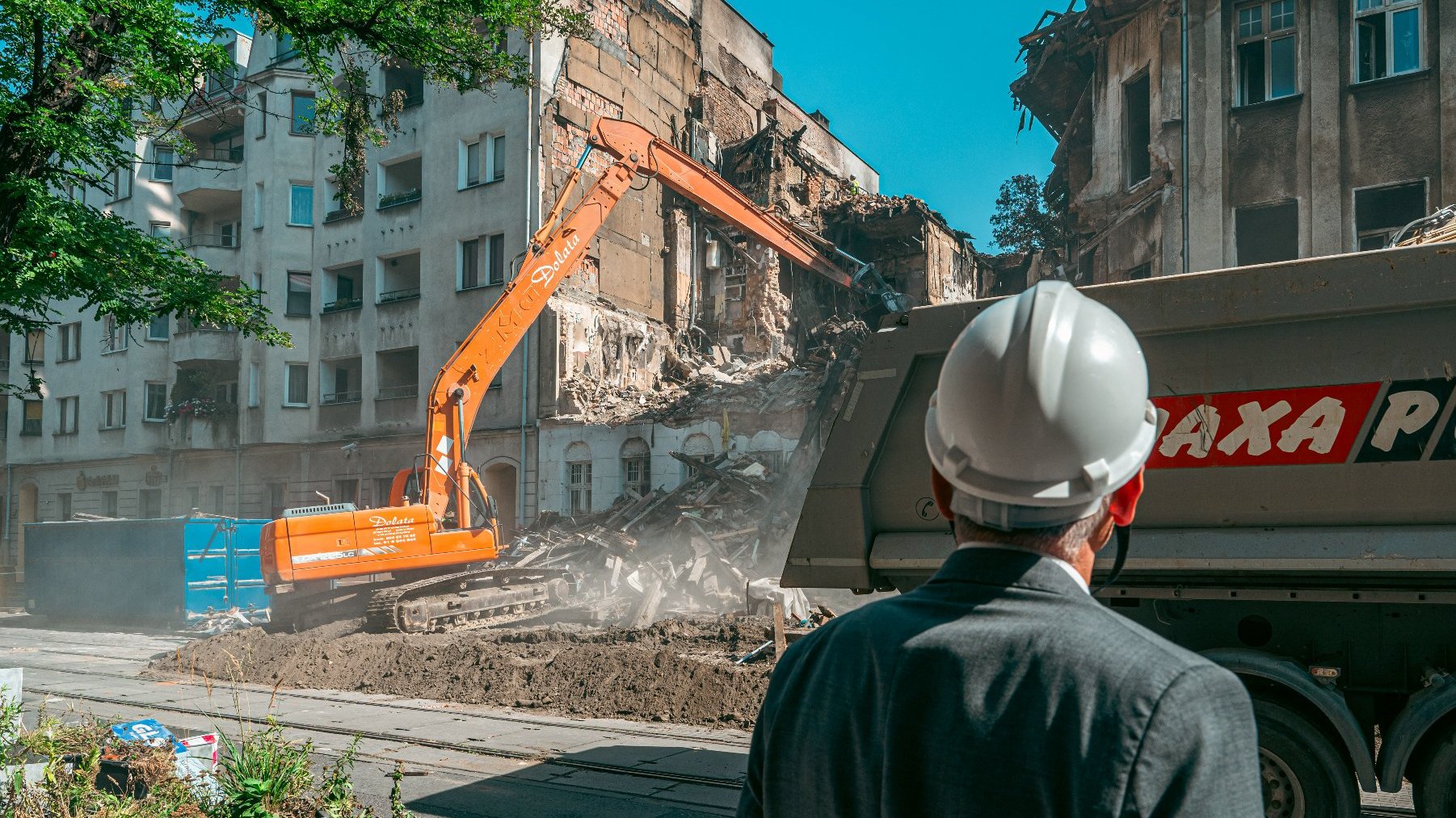 Na zdjęciu mężczyzna w kasku obserwujący rozbiórkę kamienicy