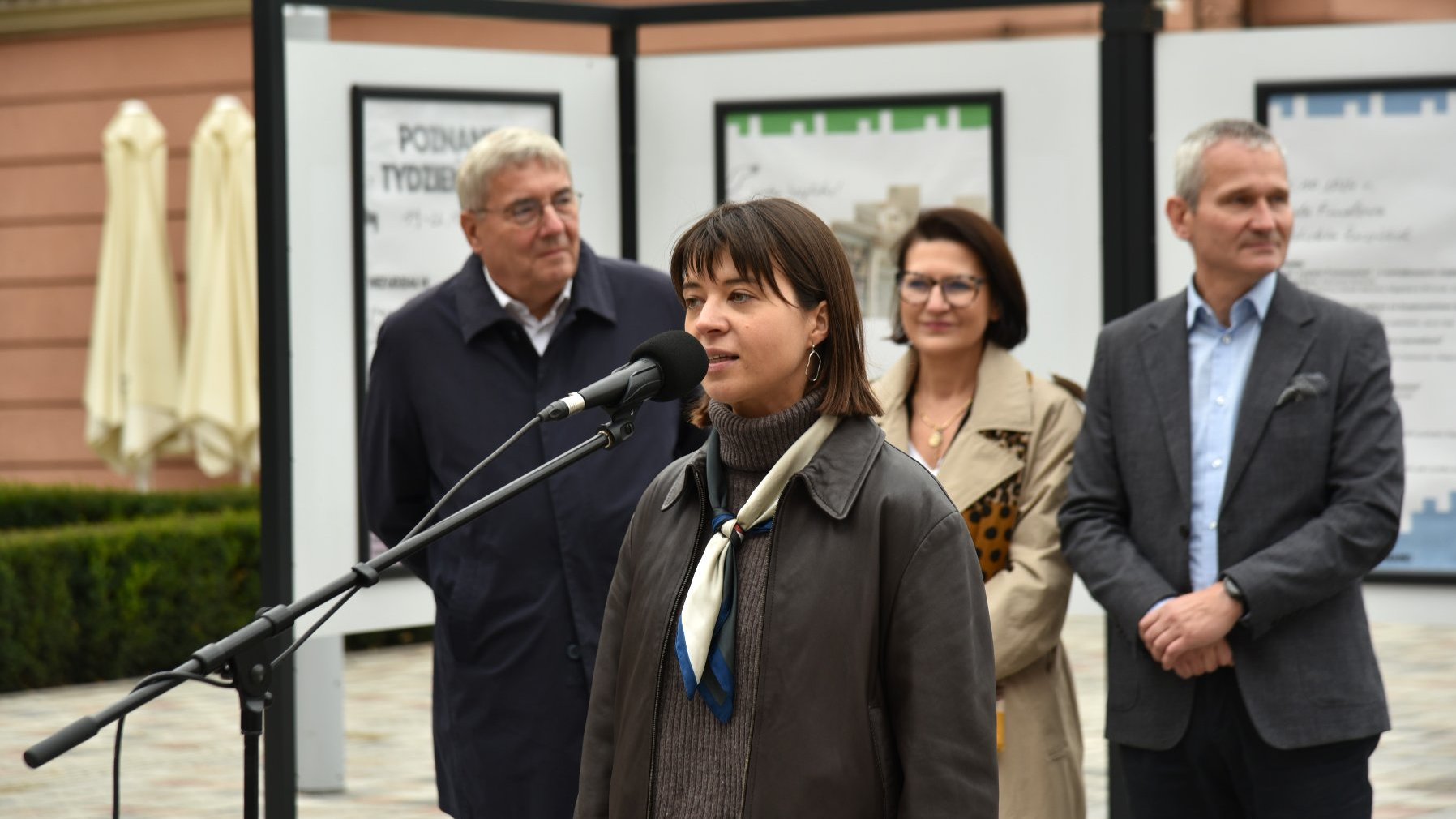 Zdjęcie przedstawiaosoby biorące udział w konferencji. Przy mikrofonie stoi przedstawicielka fundacji, współorganizatorka akcji. Za jej plecami znajduje się wystawa.