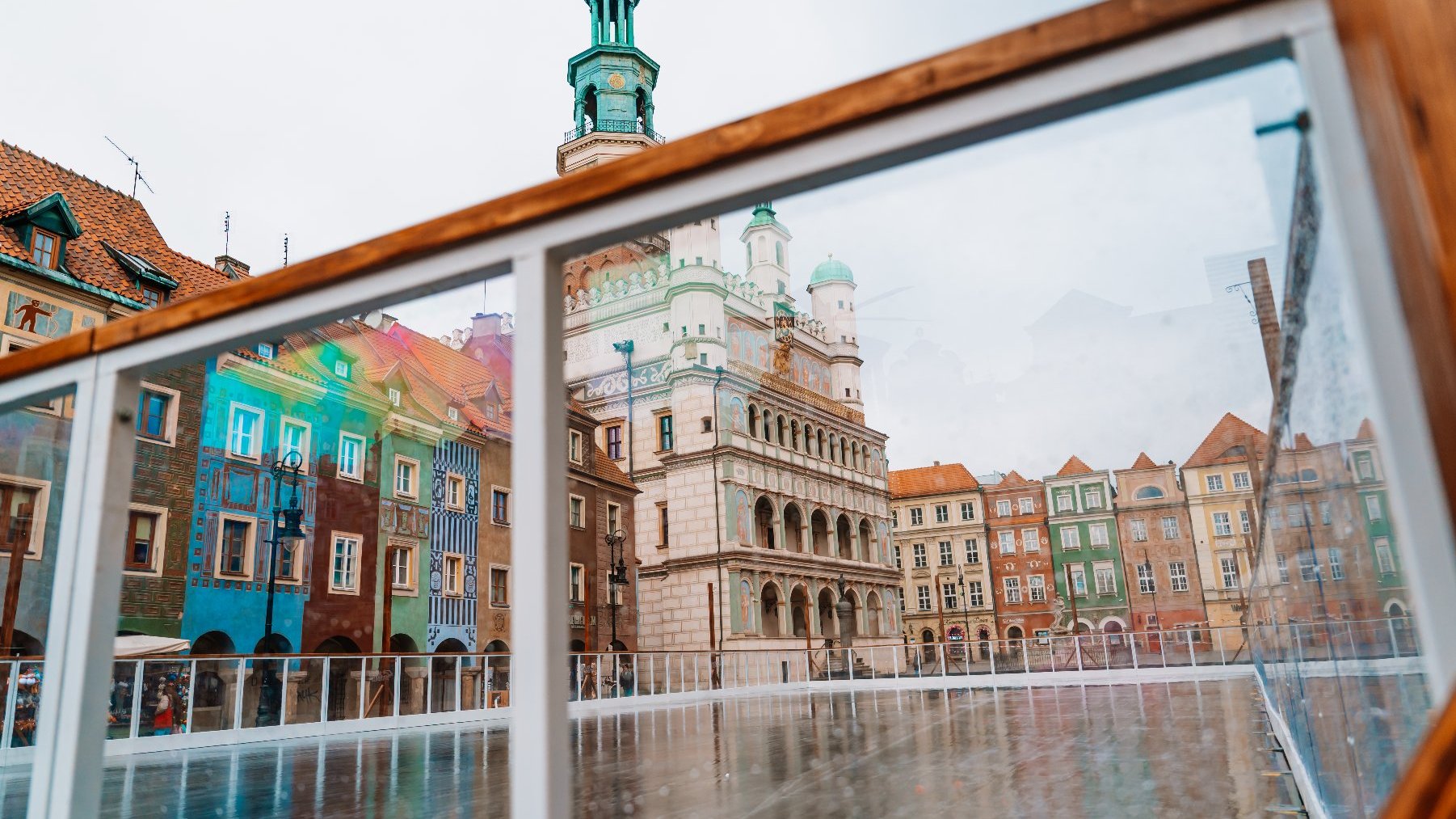 Zdjęcie przedstawia budynki na Starym Rynku widziane przez szybę powstającego lodowiska.