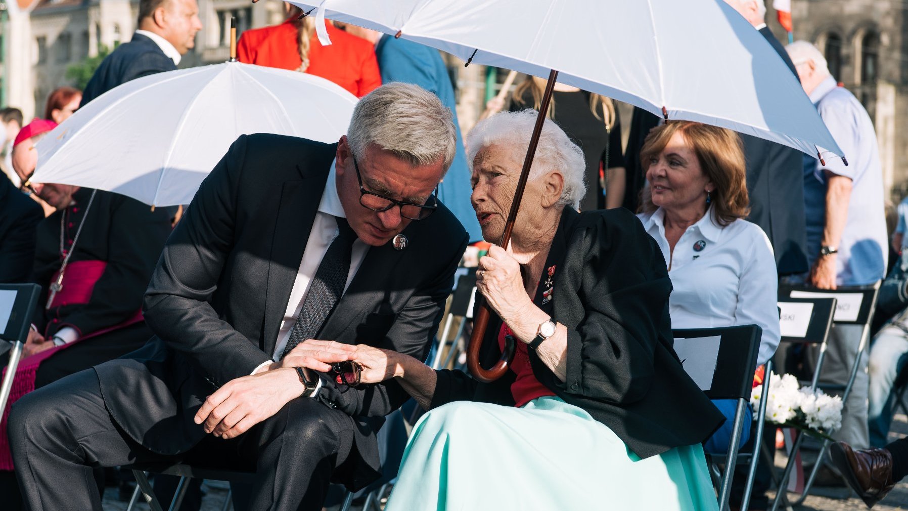 Jacek Jaśkowiak pochylajacy się ku Aleksandrze Banasiak, oboje siedzą, chroniąc się przed słońcem pod białym parasolem