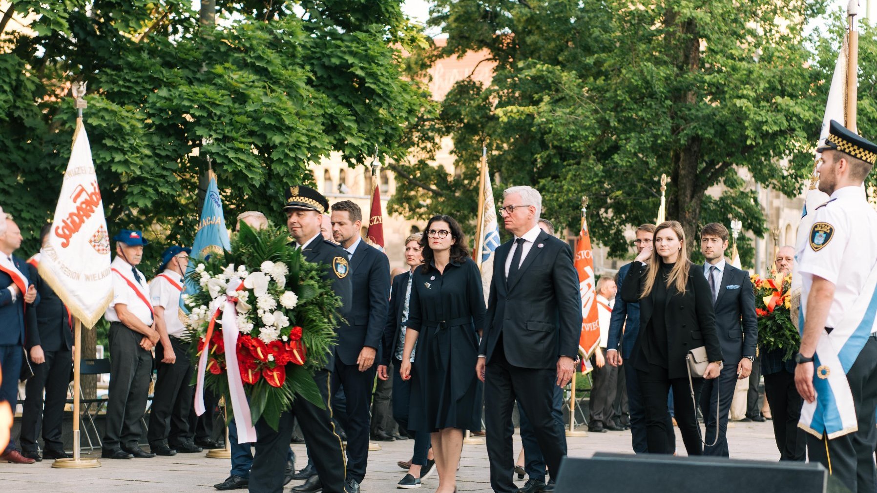 Jacek Jaśkowiak składający kwiaty razem z innymi samorządowcami, na pierwszym planie strażnik z wiązanką