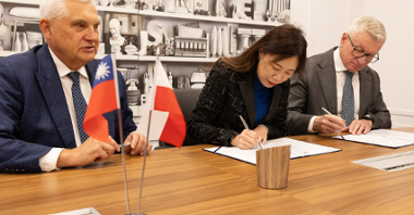 Na zdjęciu dwóch mężczyzn i kobieta za stołem, podpisują porozumienie