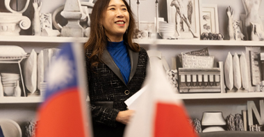 Na zdjęciu uśmiechnięta kobieta, na pierwszym planie flagi Polski i Tajwanu