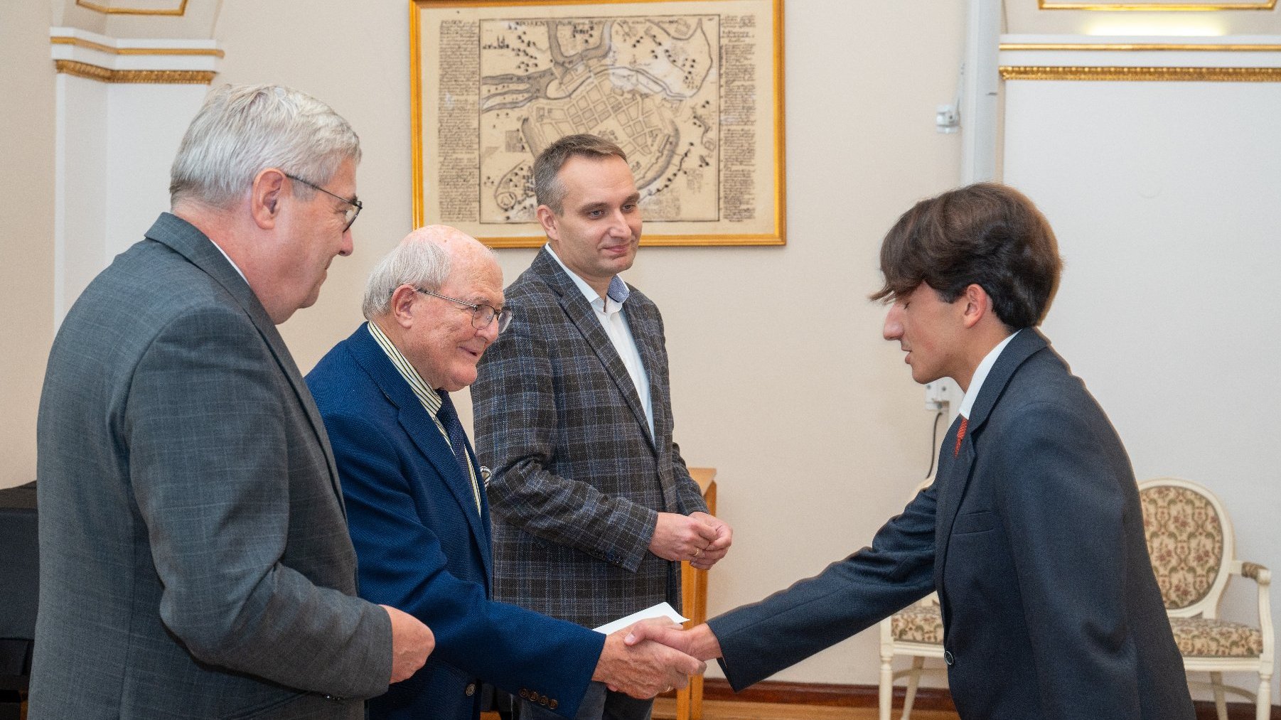 Zdjęcie przedstawia trójkę mężczyzn i młodego chłopaka podającego im rękę.