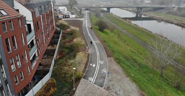 Wartostrada - nowy odcinek drogi rowerowej i pieszej, w tle most, po lewej budynek, po prawej rzeka Warta.