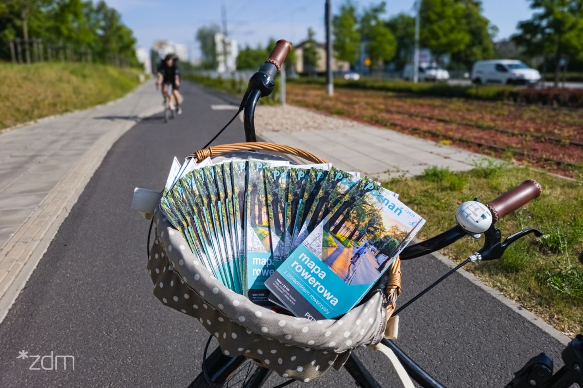 Zdjęcie, rower stoi na ścieżce rowerowej. W koszyku zawieszonym na kierownicy znajduje się plik map rowerowych Poznania. - grafika artykułu