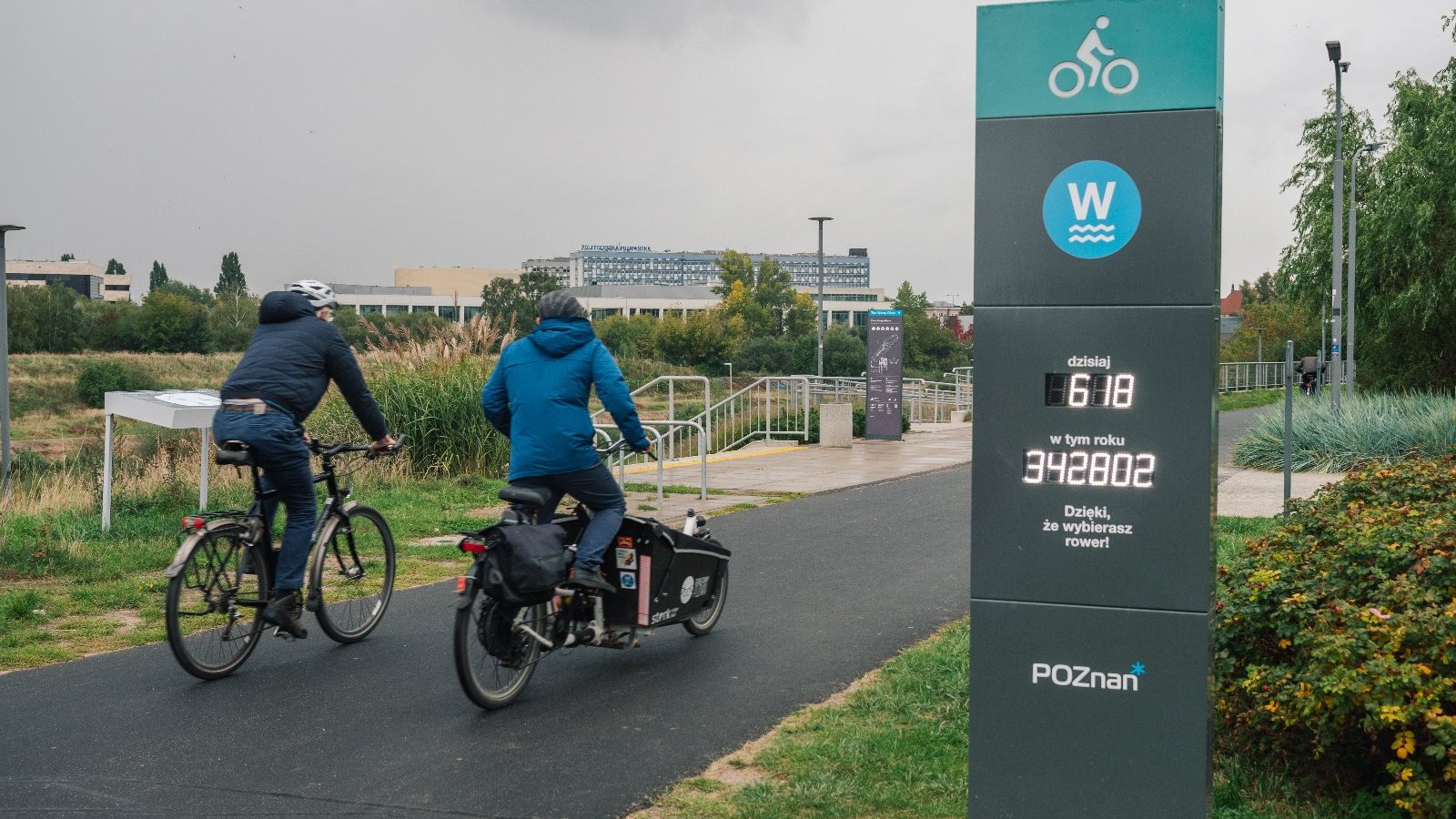 Zdjęcie, dwoje rowerzystów na trasie rowerowej, obok licznik rowerowy.