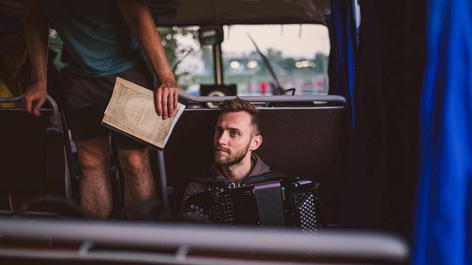 Zdjęcie przedstawia mężczyznę, który gra na akordeonie w autobusie.