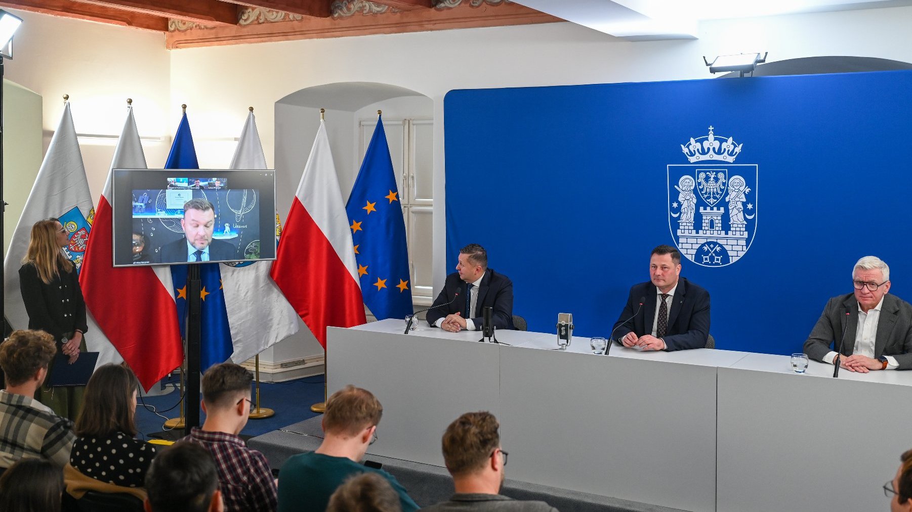 Na zdjęciu konferencja prasowa, widać mówców za stołem i dziennikarzy