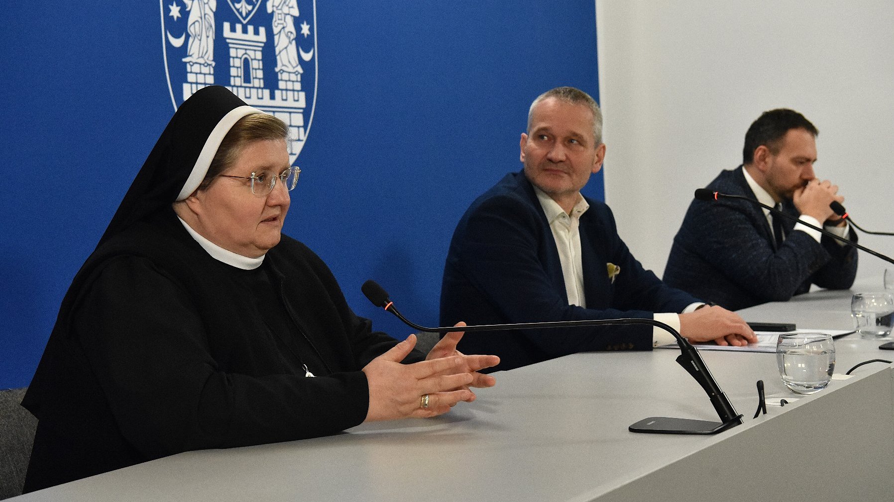 Na zdjęciu trzy osoby za stołem konferencyjnym, na pierwszym planie zakonnica