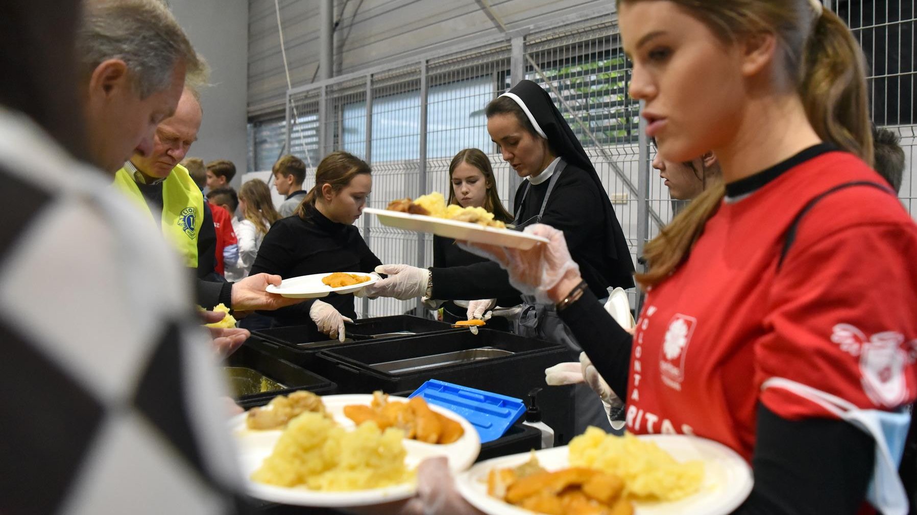 Na zdjęciu wolontariusze i zakonnica, nakładający jedzenie na talerze