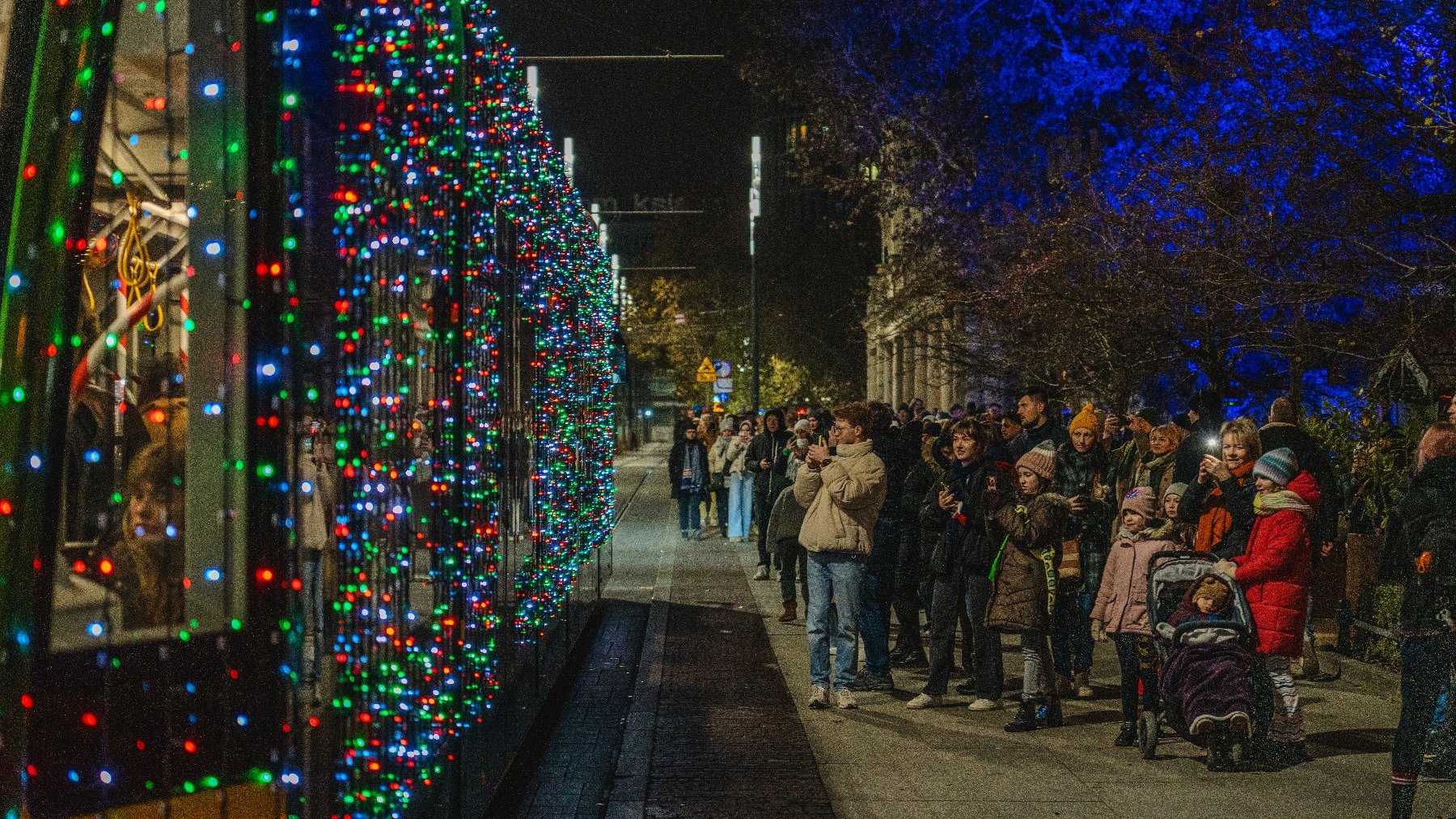 Zdjęcie przedstawia podświetlony lampkami tarmwaj oraz tłum oglądajacych go ludzi.