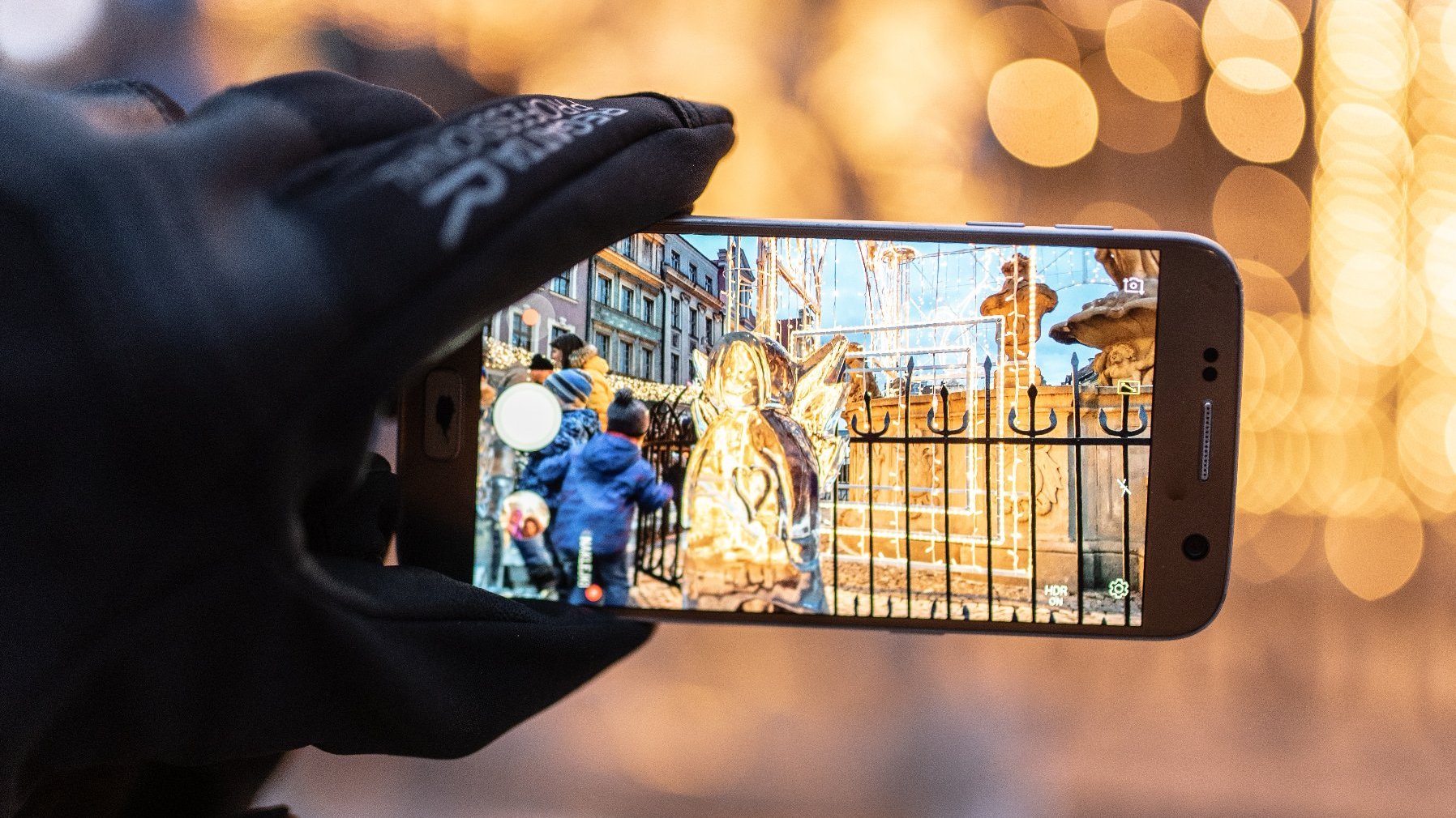 Zdjęcie przedstawia lodową rzeźbę i ludzi widziani w ekranie telefonu.