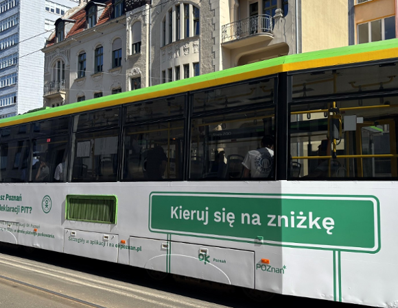 Pozostawienie cen Biletów Metropolitalnych bez zmian to nie tylko finansowa ulga dla pasażerów... Tramwaj oklejony naklejkami z OK Poznań, jadący pomiędzy kamieniczkami.