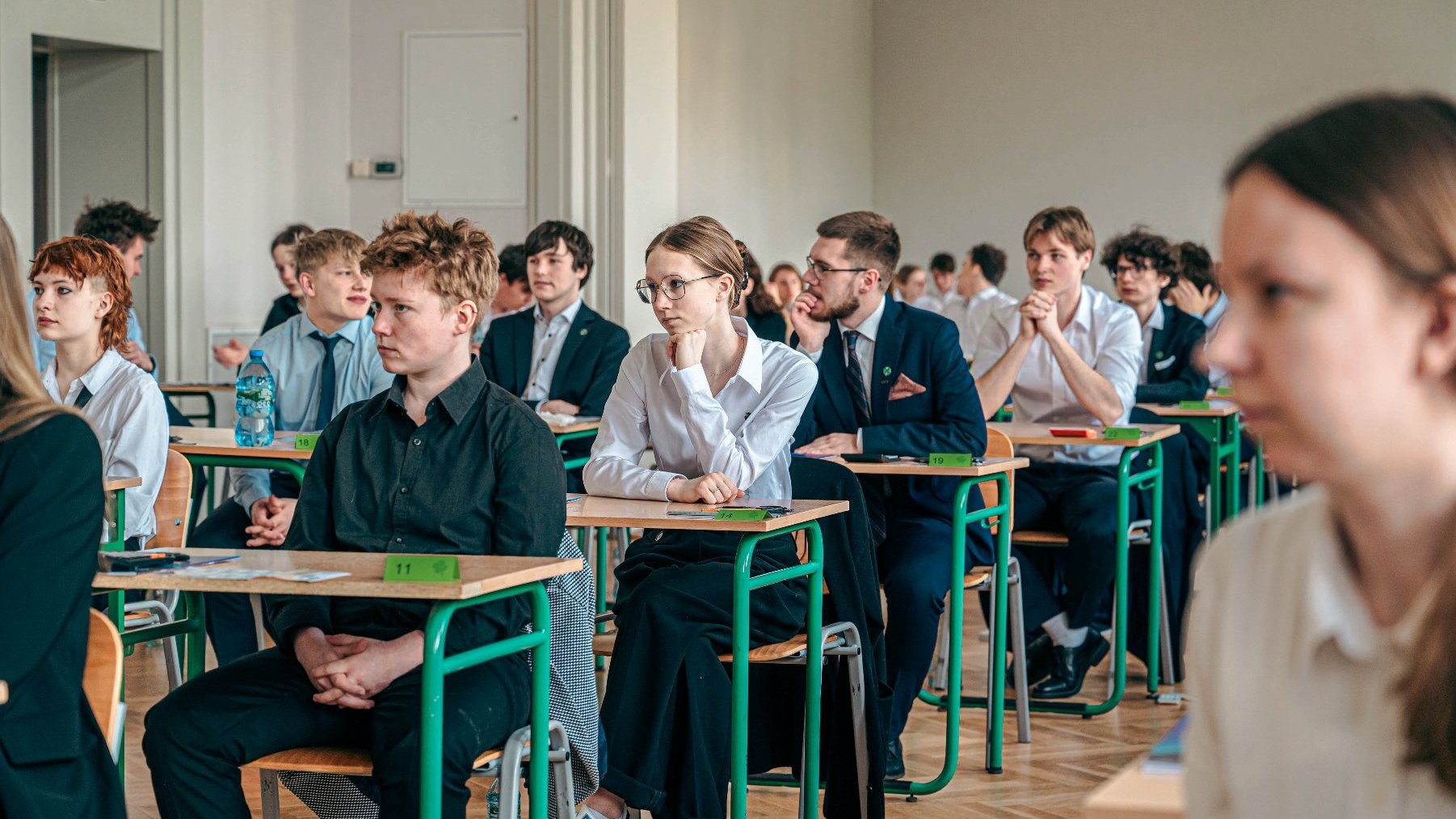 Zdjęcie przedstawia maturzystów siedzących w ławkach.