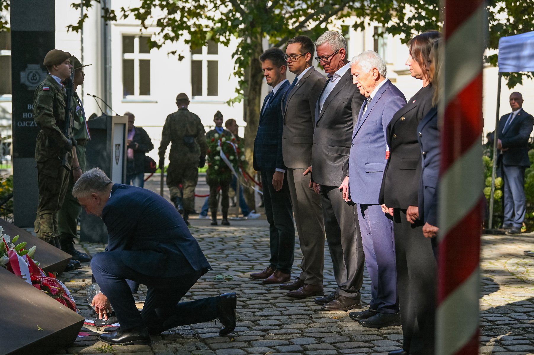 Zdjęcie przedstawia ludzi podczas składania kwiatów. - grafika artykułu