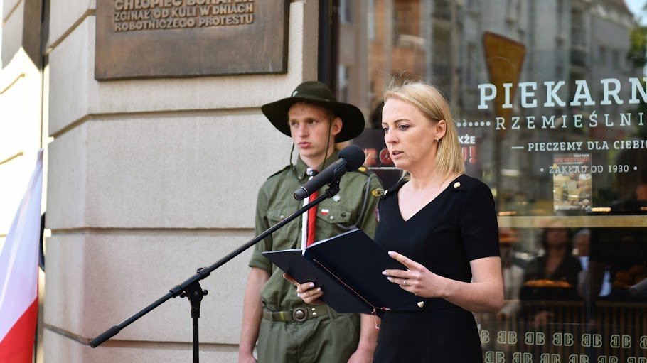 Na zdjęciu kobieta przy mikrofonie, za nią harcerz