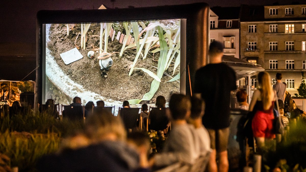 Zdjęcie przedstawia ludzi oglądających film w plenerze.