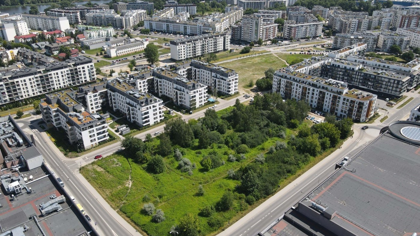 Na zdjęciu zielony plac otoczony blokami, widziany z lotu ptaka