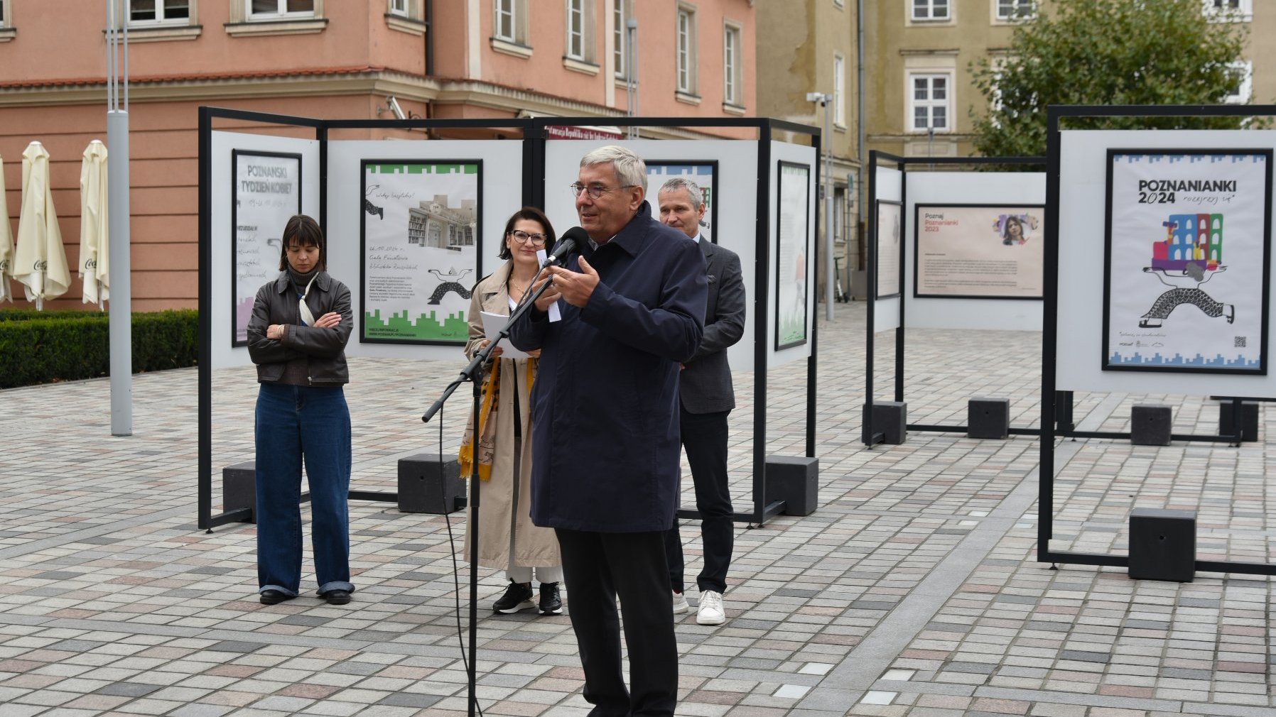 Zdjęcie przedstawiaosoby biorące udział w konferencji. Przy mikrofonie stoi przewodniczący rady miasta. Za jego plecami znajduje się wystawa.