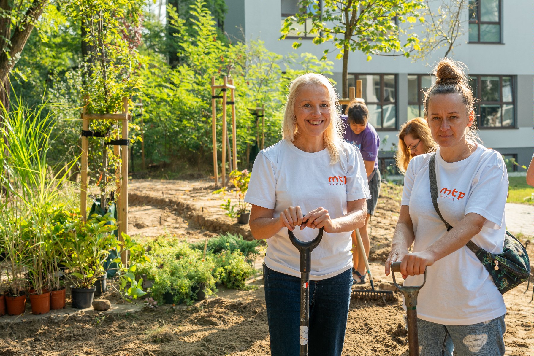 Na zdjęciu dwie uśmiechnięte wolontariuszki z łopatami, w tle drzewa - grafika artykułu