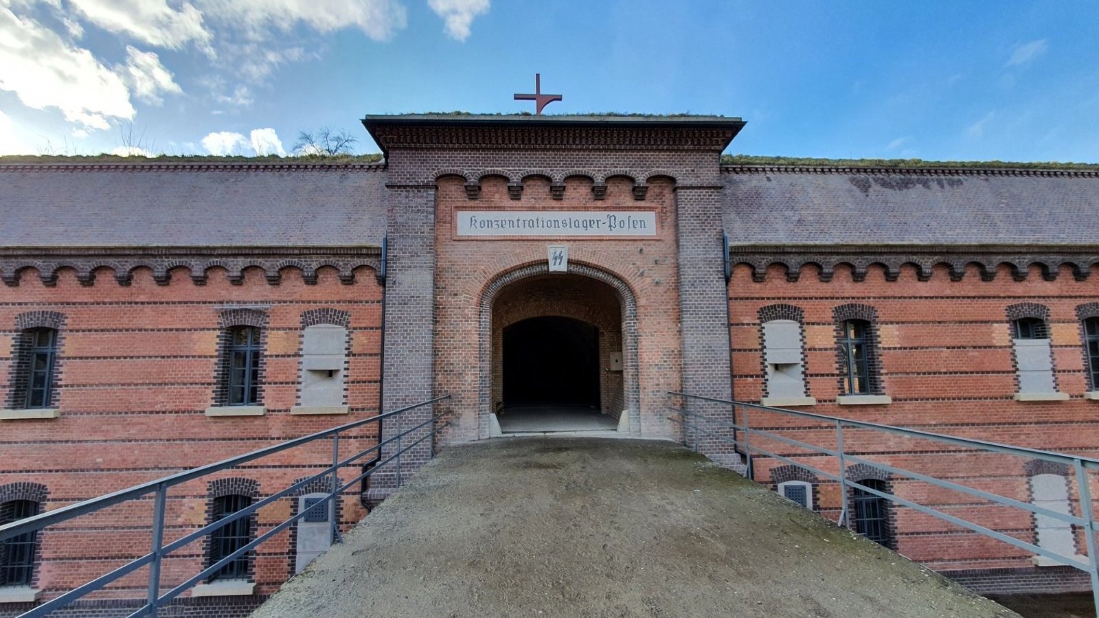 Wejście do Fortu VII. Prowadzi do niego długi most, na jego końcu jest budynek i brama w kolorze cegły.