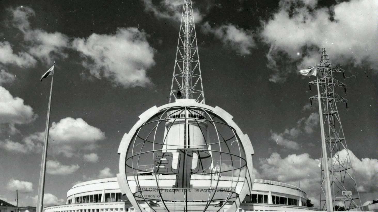 Black and white photo of a fair building - a spire which is a symbol of Poznań fair. In a foreground a sphere bearing the fair logo.