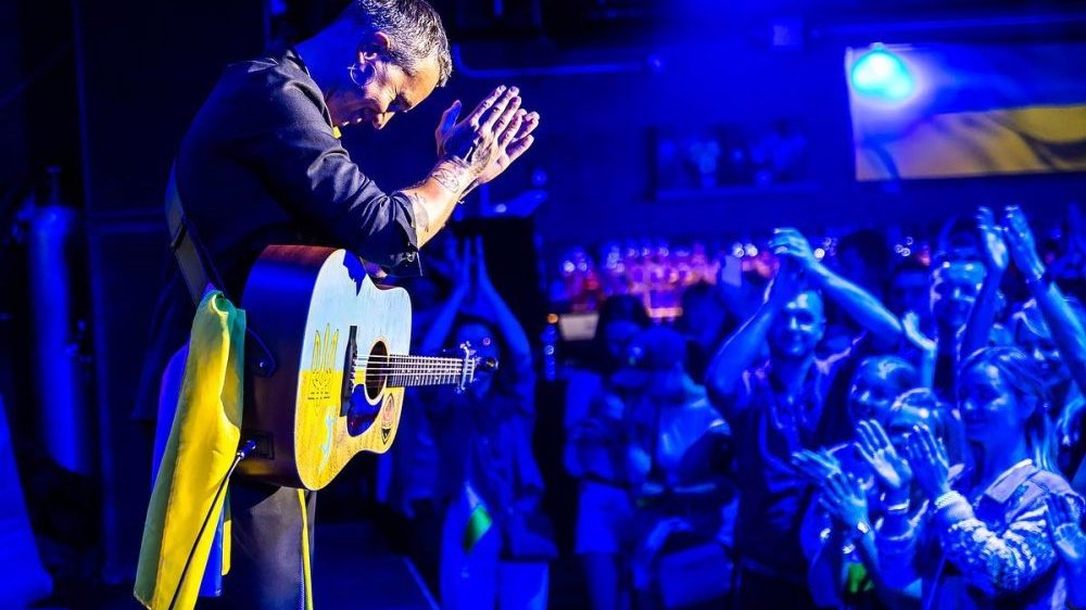 Photo of Sergiy Babkin with the guitar performing on stage; on the right - people who clap their hands. - grafika artykułu