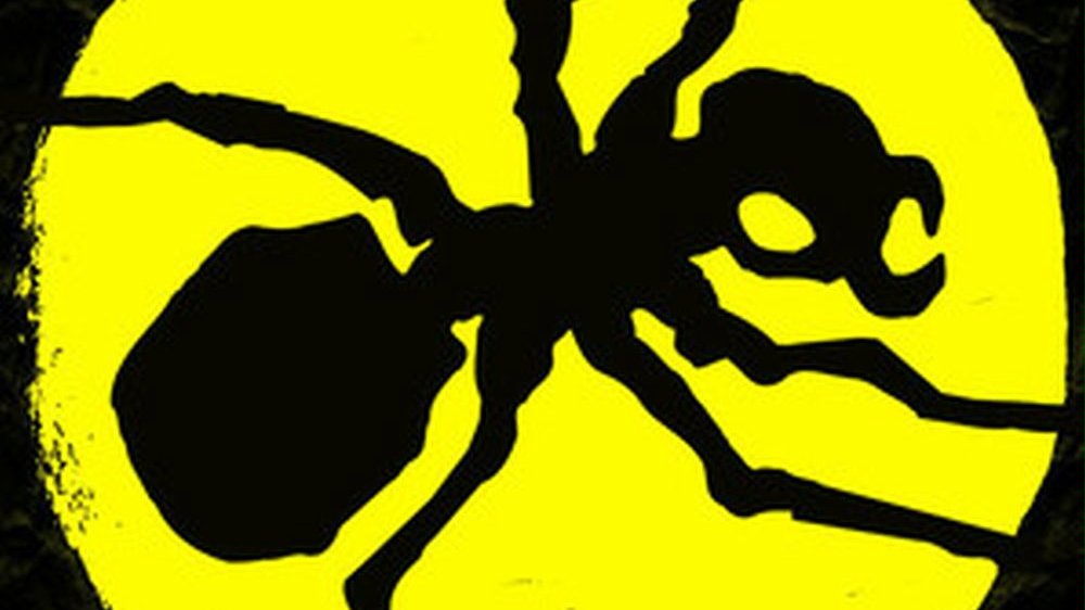 Black ant on a yellow circle. Black background.