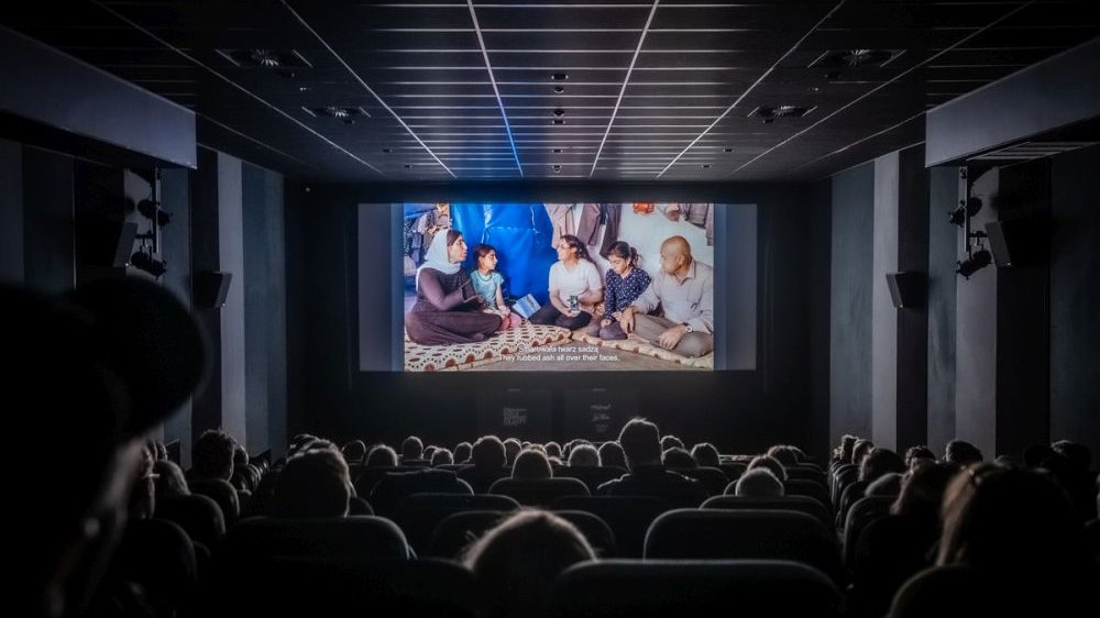Audiences in the cinema watch a movie on a big screen. It is dark, the room is illuminated only by the light from the screen.