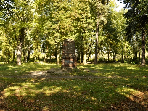 Stary nagrobek z cegieł. Dookoła trawa i wysokie drzewa