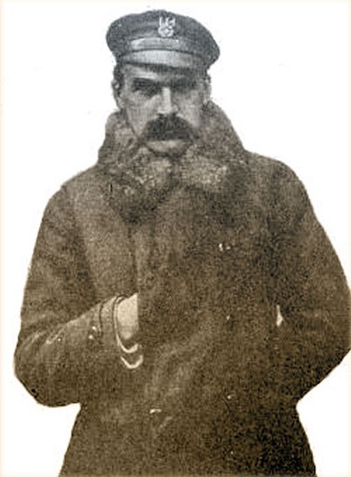 Archiwalne zdjęcie Józefa Piłsudskiego, pozującego w wojskowym płaszczu i czapce, z prawą dłonią schowaną w poły płaszcza i lewą schowaną za plecami.