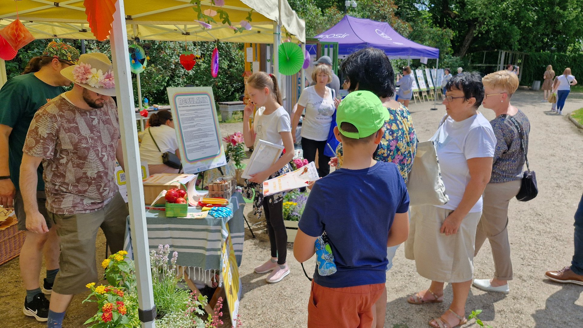 akcje edukacyjne - relacja z zielonych warsztatów w ramach "Akademii Zielony Poznań" - "Zieloni od 30 lat - jubileusz z klimatem" - 25 maja 2024 r. Park Wilsona,gra terenowa pt."Od Robala do Superbohatera".Miłośnicy kwiatów mogli zainspirować się roślinnymi kompozycjami, które na dodatek były stołówką dla pożytecznych owadów. Wielbiciele roślin skorzystali z warsztatów z tworzenia wiszących zielonych kul - kokedam,na zdjęciu widoczne kolorowe kwiaty, uczestnicy z kartami do gry