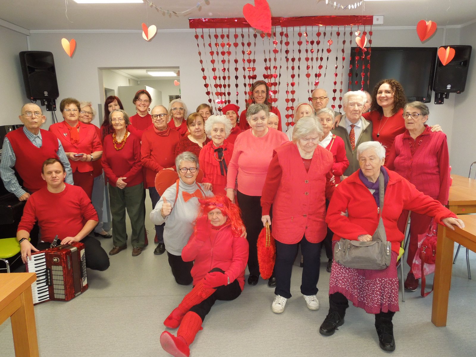 grupa kilkudziesięciu seniorów i pracowników ubranych na czerwono pozuje do zdjęcia - grafika artykułu