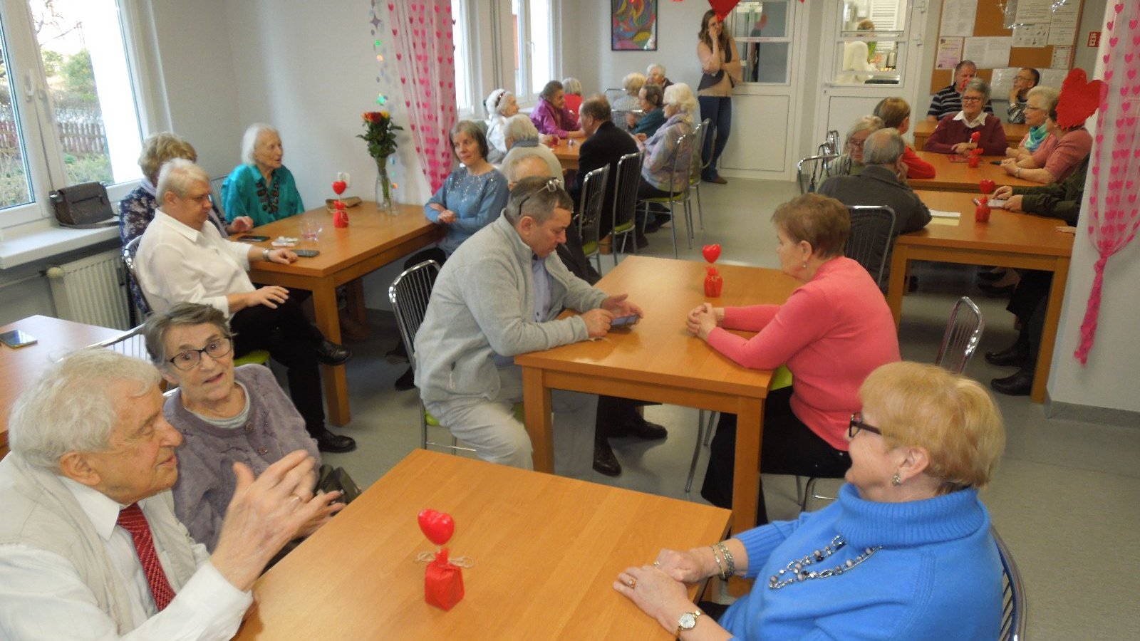 na sali seniorzy siedzą przy stolikach i rozmawiają