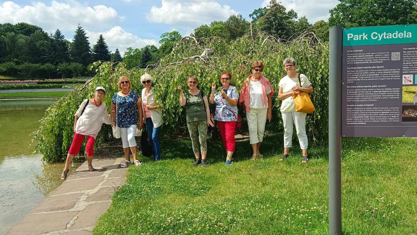 Grupa uśmiechniętych kobiet stojąca przy stawie w parku