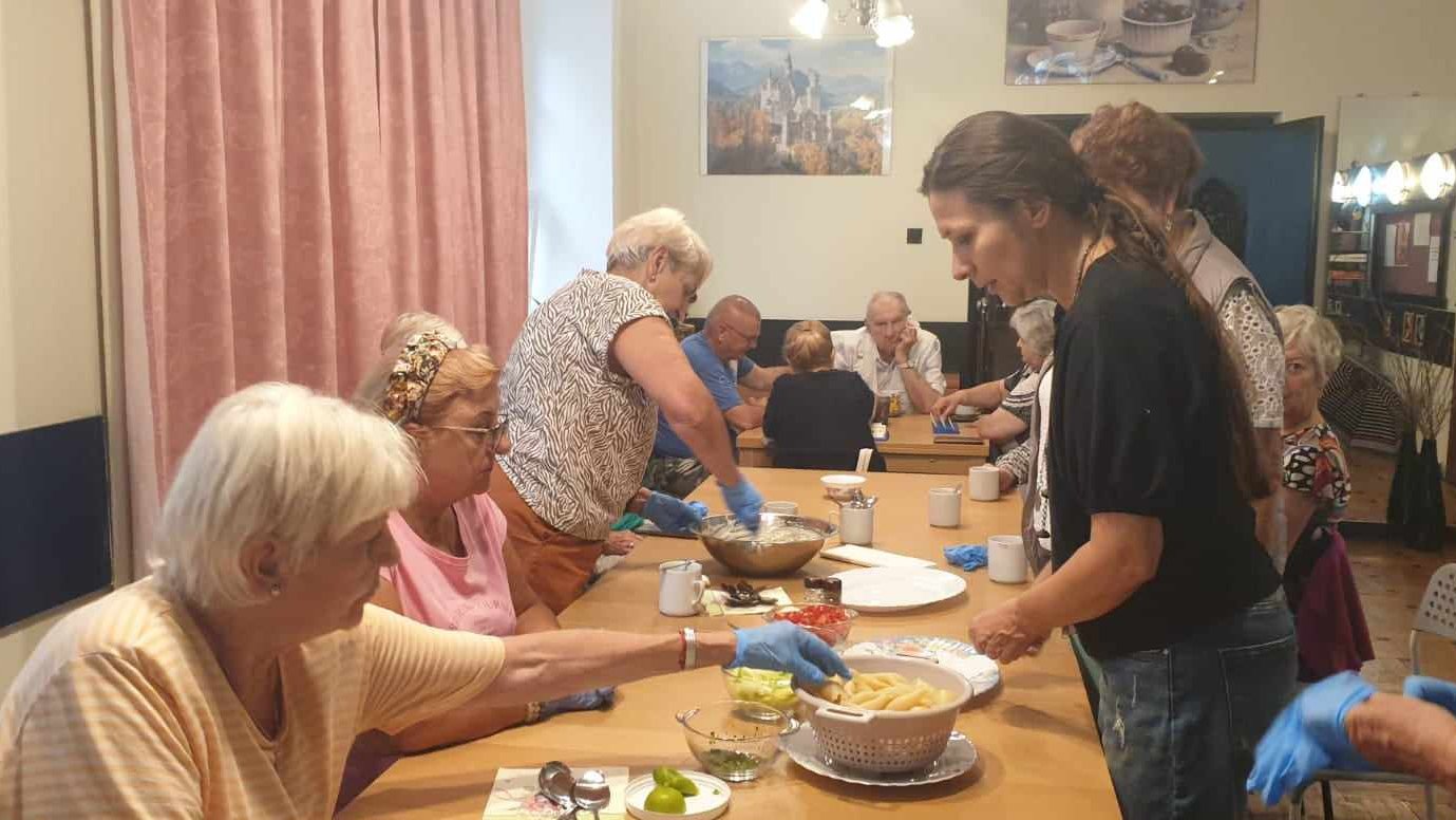 Seniorki wraz z instruktorem wypełniają muszle przygotowanym farszem.