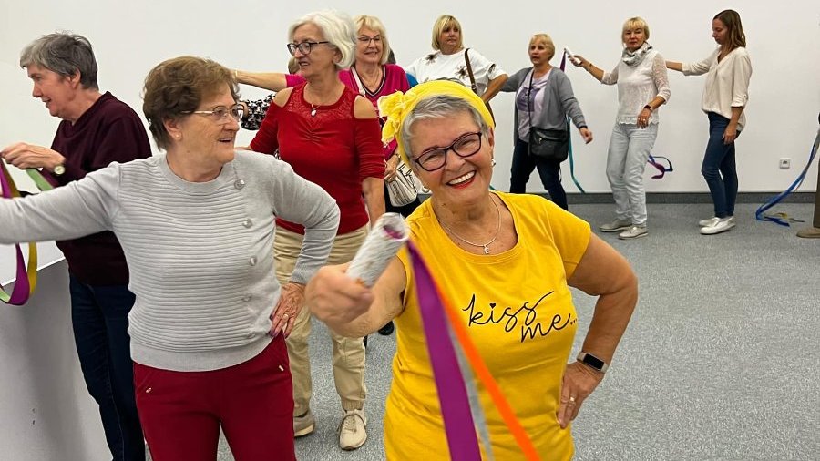 tańcząca grupa seniorów, na pierwszym planie uśmiechnięta kobieta