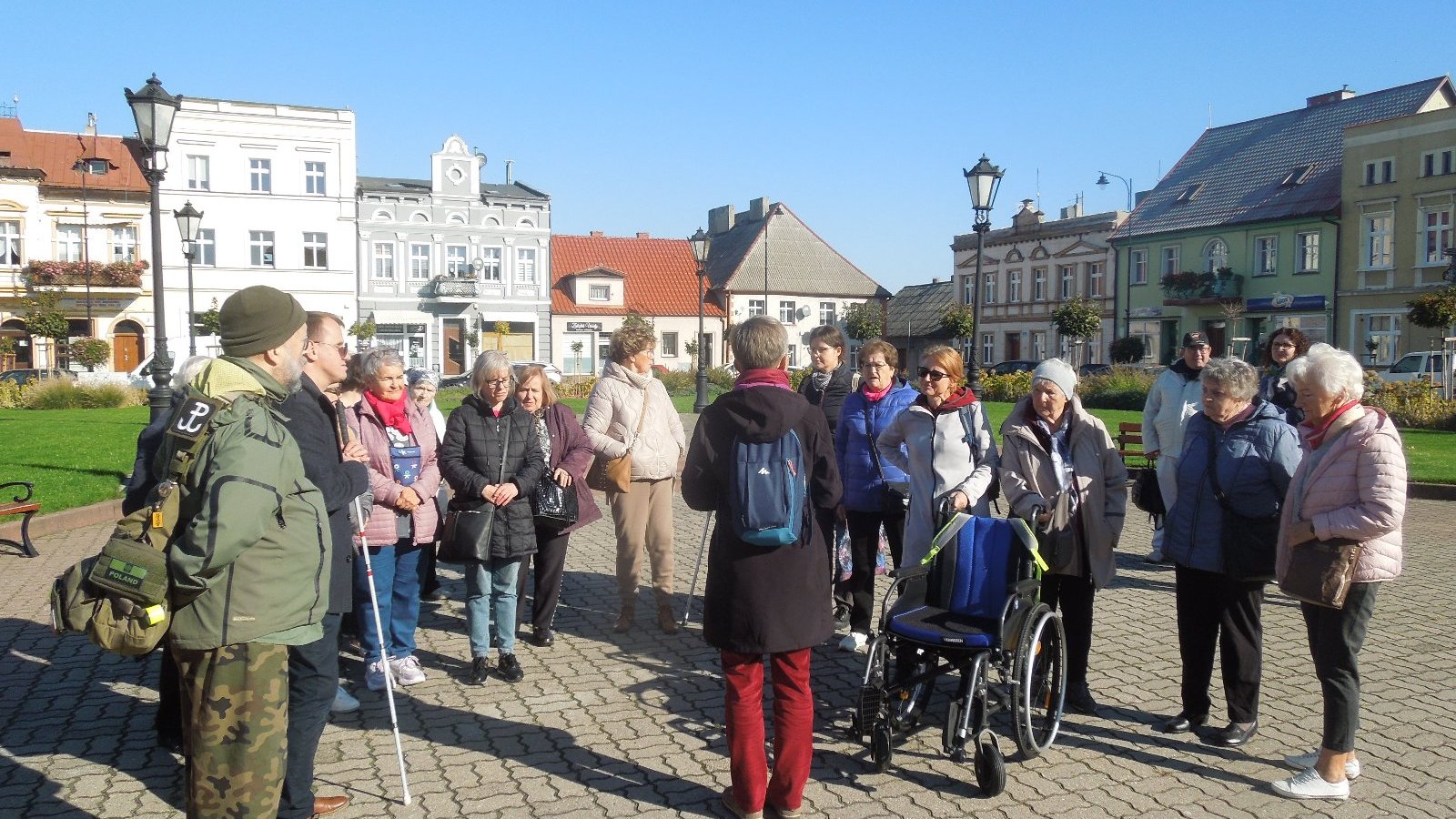 grupa osób stoi na rynku miasta i słucha przewodnika