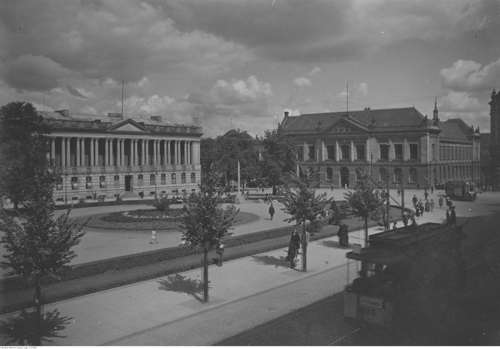 Czarno-białe zdjęcie. Fotograf, stojąc na podwyższeniu, pokazał Plac Wolności, którym przechadzają się spacerowicze. Widać budynek Biblioteki Raczyńskich i stojący po drugiej stronie ulicy gmach Muzeum Narodowego. - grafika artykułu