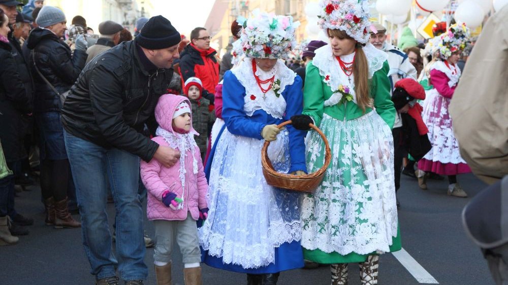 Dwie dziewczyny w kolorowych strojach bamberskich idą ulicą wśród tłumu ludzi. Podchodzi do nich mężczyzna z dzieckiem.