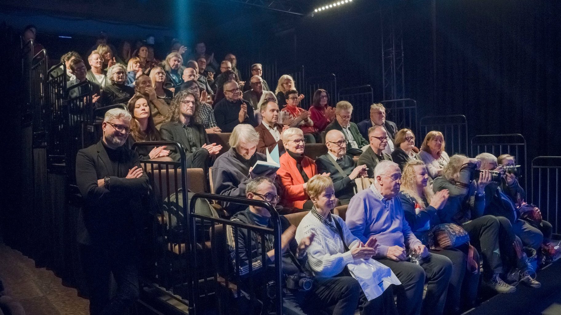 Licznie zgromadzona publiczność. Kilkadziesiąt ludzi siedzących w fotelach teatralnych obserwujących rozmowę.